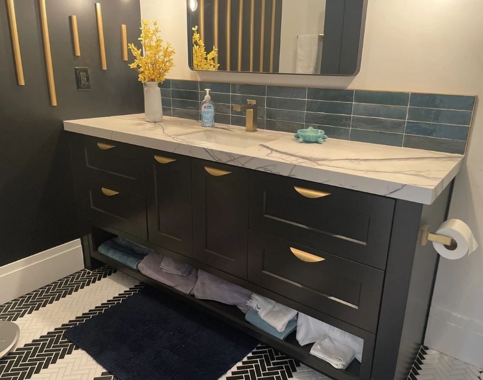 Dark vanity with gold hardware, white countertop, blue backsplash, and decorative wall.