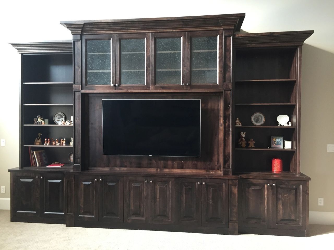 Dark stained wooden entertainment center with TV, glass-fronted cabinet, and side bookshelves.