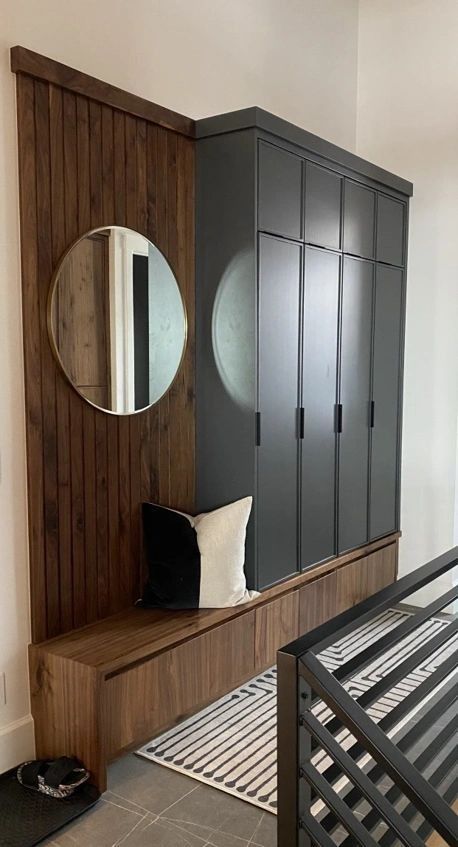 A modern entryway with dark wood paneling, built-in storage, a bench, and a round mirror.
