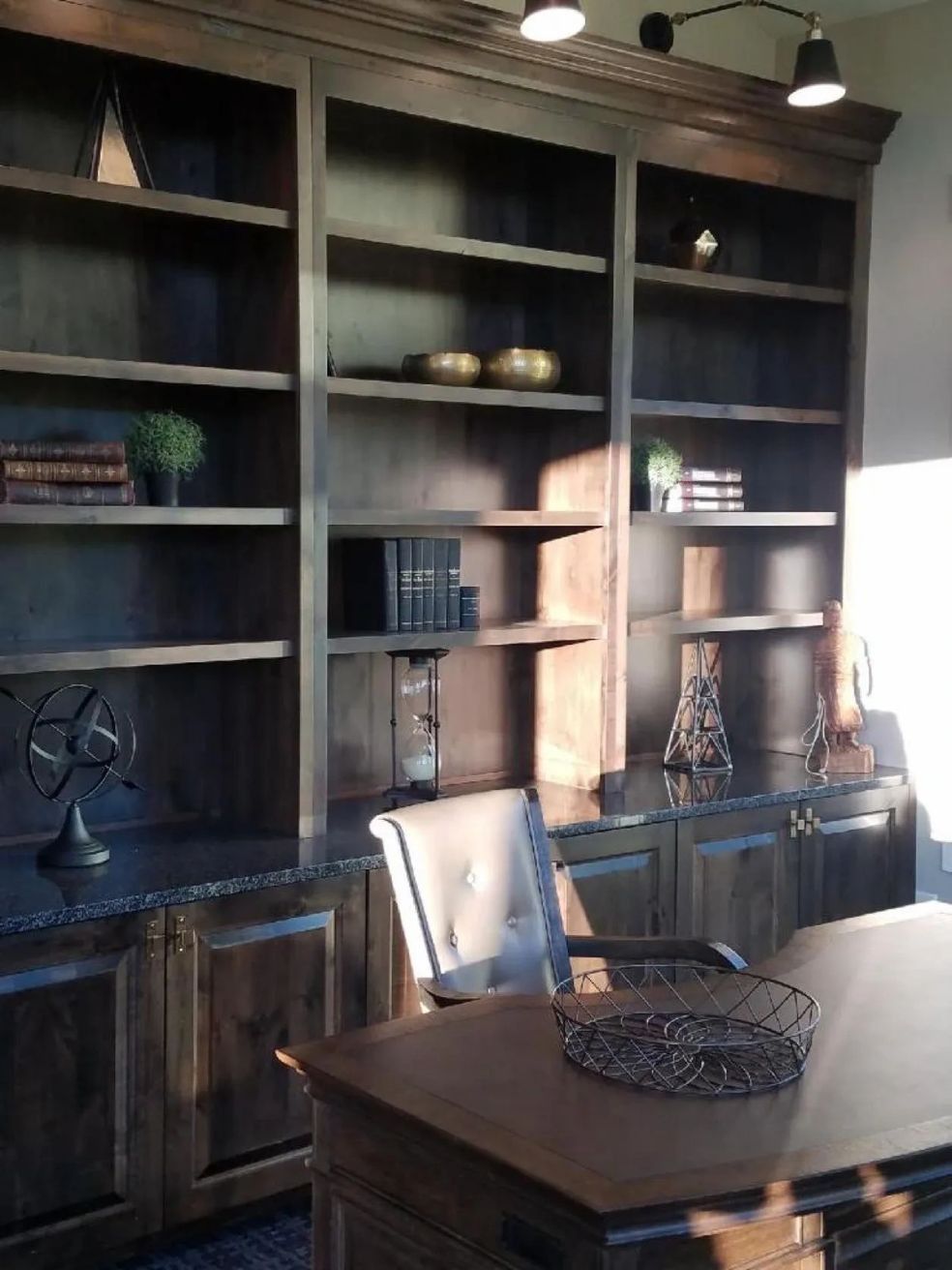 Wooden built-in office desk with bookshelves, desk, and chair; items on shelves, sunlight.