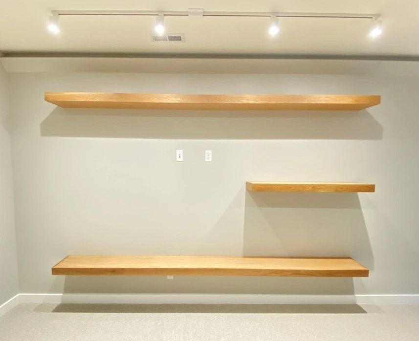 Light wood floating shelves on a light gray wall, with a white ceiling and a track lighting system.