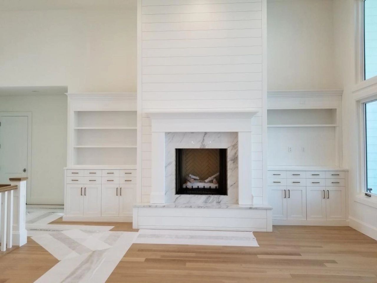 White fireplace with built-in shelving and cabinets in a bright, spacious room with hardwood floors.