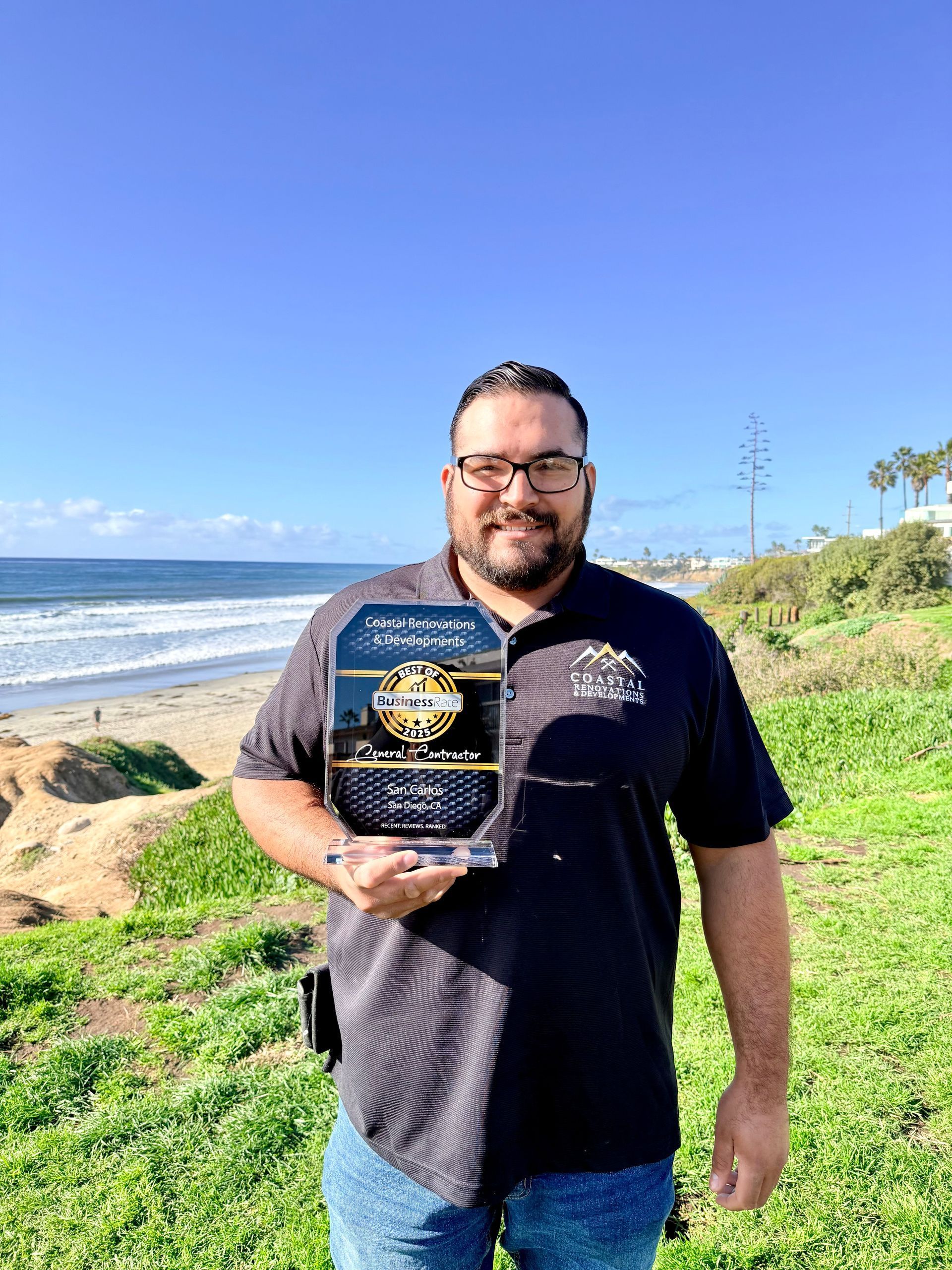 Man holding a trophy with the ocean in the background on a sunny day.