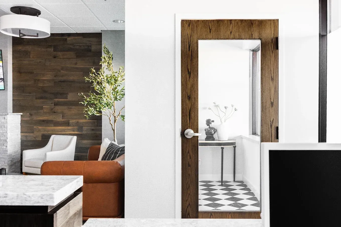 Interior with wood-framed doorway, white walls, and a living area with a brown couch and wooden accent wall.