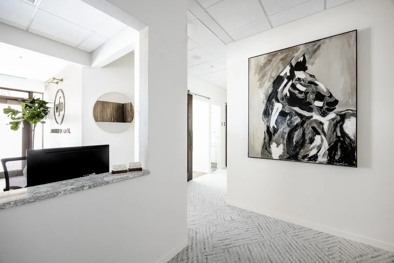 Modern office reception area with abstract horse painting, white walls, and gray carpet.