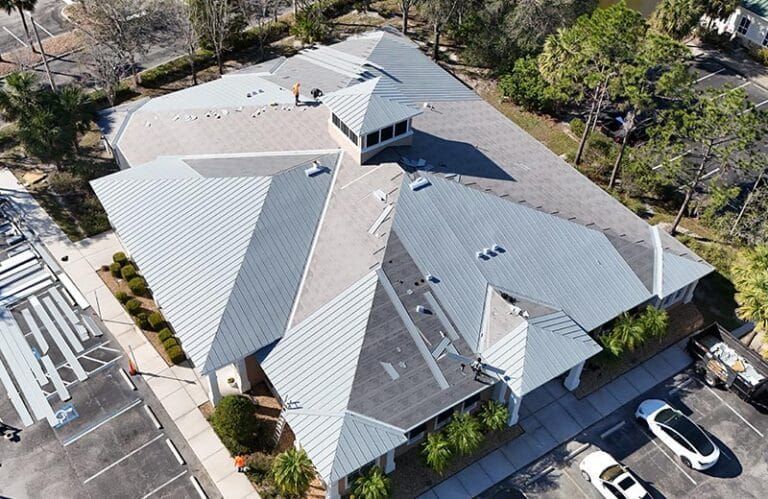 Aerial view of a building with a complex multi-level gray roof and a surrounding parking lot with cars.