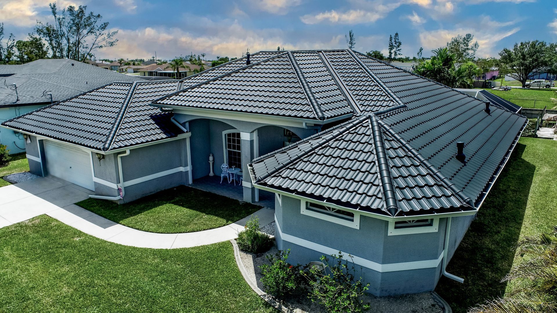 Blue house with dark gray tile roof, green lawn, and bright sky.