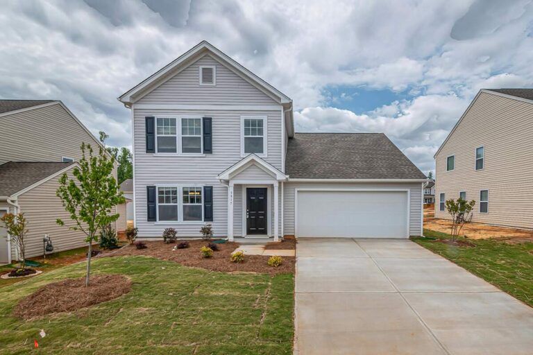 Two-story light gray house with a white garage door and black shutters. Cloudy sky in the background.