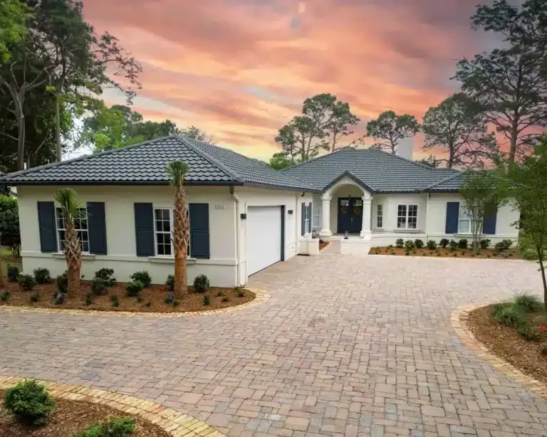 White house with blue shutters and driveway at sunset.