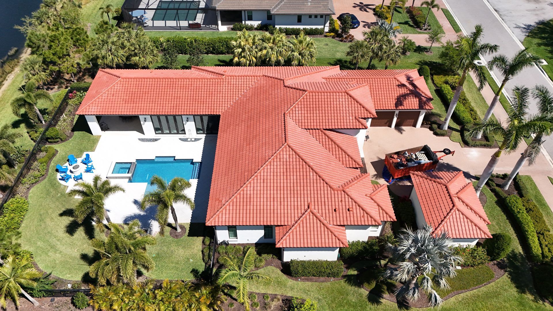 Aerial view of a luxury house with a red tile roof, pool, and a car in the driveway on a sunny day.