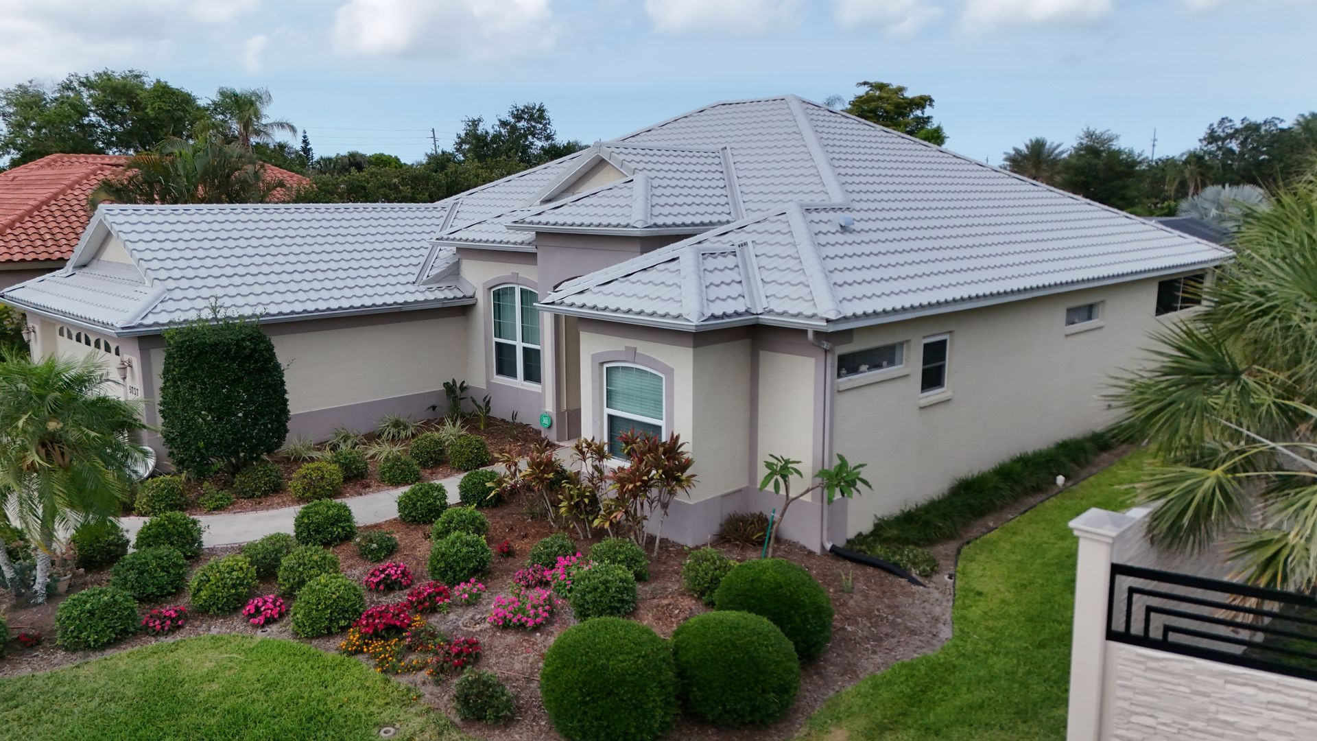House with light gray roof, beige walls, and well-manicured landscaping with colorful flowers and bushes.