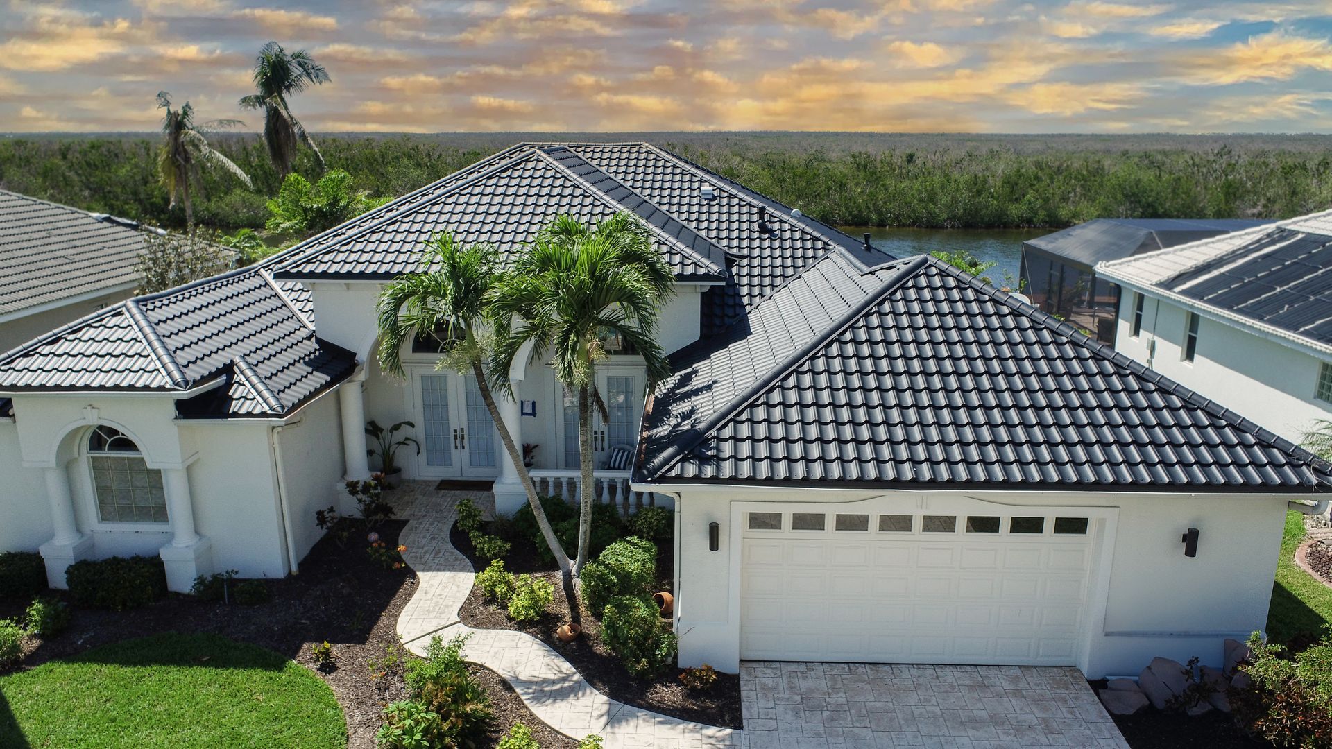 White house with black tile roof, palm trees, and waterfront view.