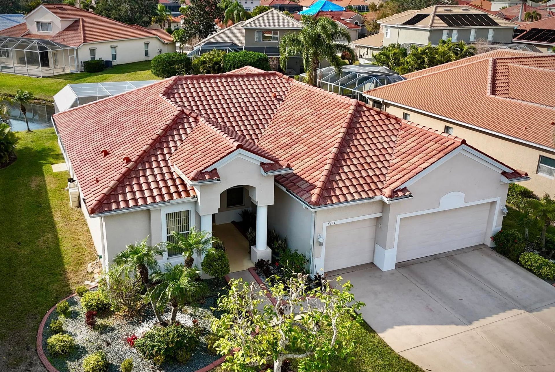 A two-story stucco house with a red tile roof. Palm trees and a driveway are in view.