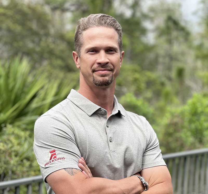 Man with crossed arms, wearing a gray polo shirt. He has a slight smile and is outdoors.