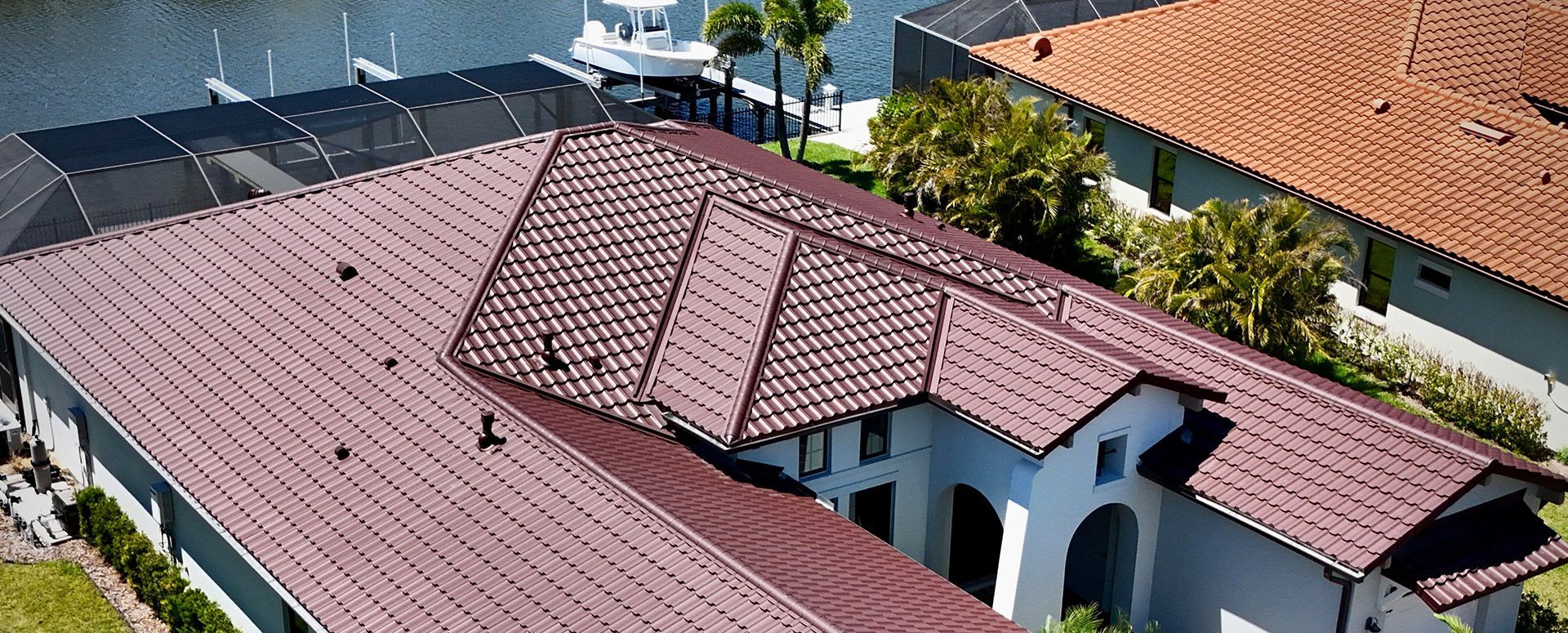 Aerial view of houses with red-tile roofs next to a waterway with boats, sunny day.