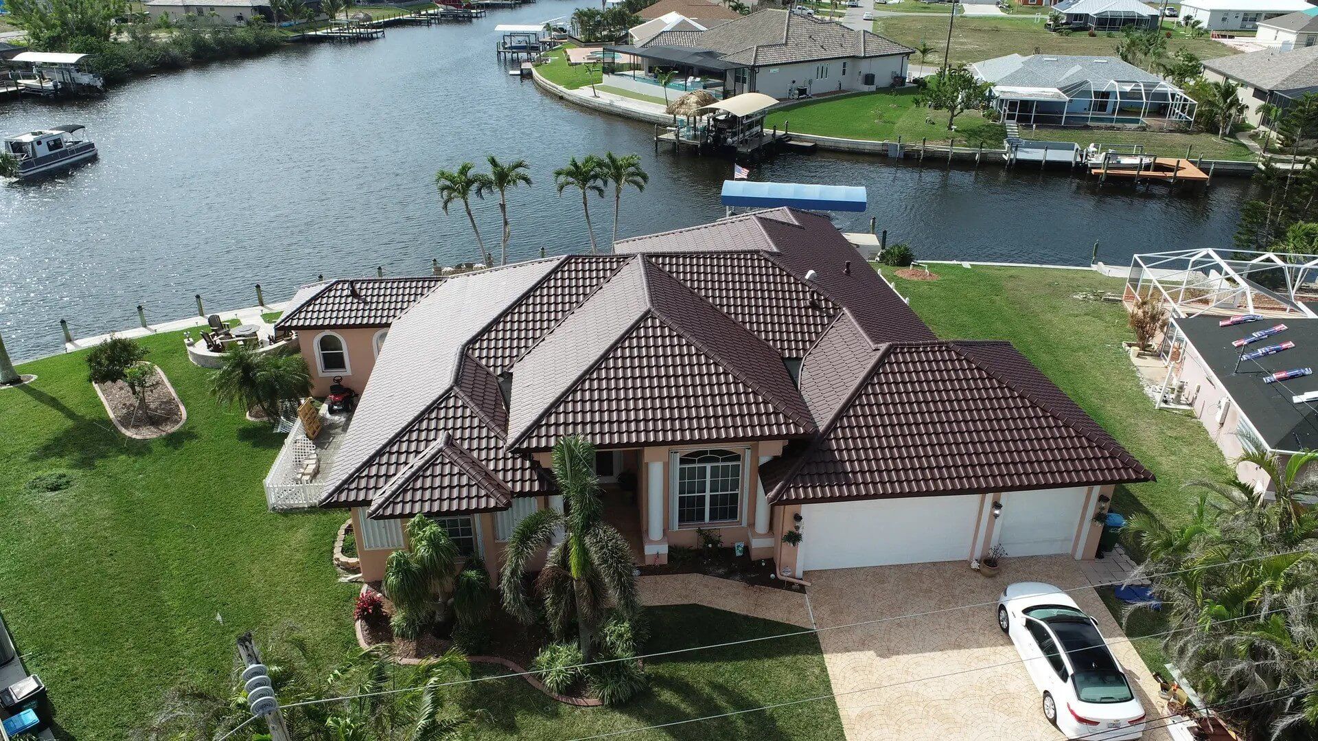 House with brown tile roof on canal, white car in driveway.