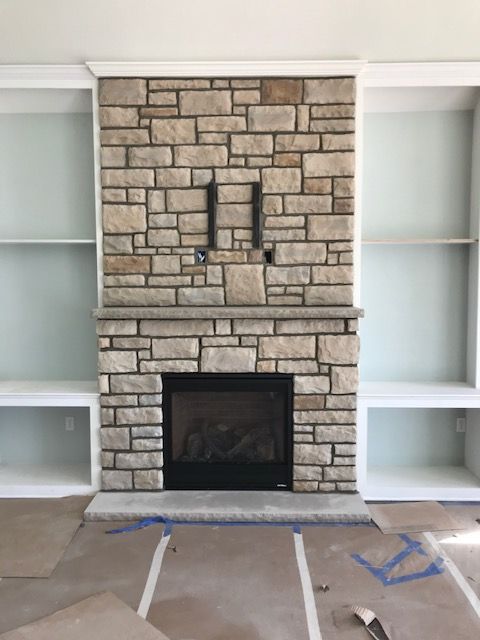A living room with a stone fireplace and shelves