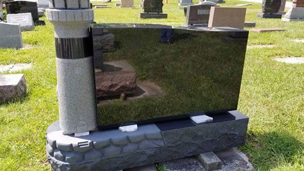 A black gravestone with a lighthouse on it is in a cemetery.