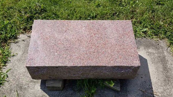 A pink granite bench is sitting in the grass in a cemetery.