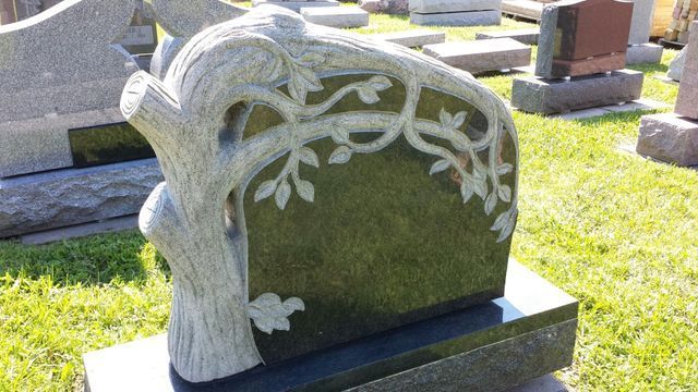 A gravestone with a tree carved into it is in a cemetery.