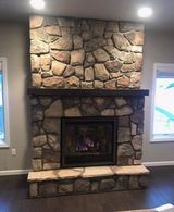 A living room with a stone fireplace and a window.