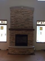A large stone fireplace in a living room with two windows.