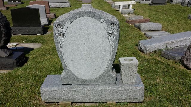 A gravestone in a cemetery with a vase in front of it.