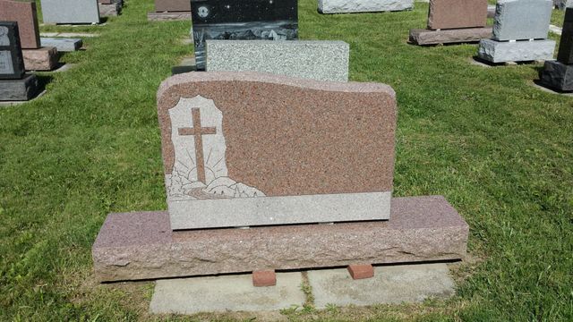 A gravestone with a cross on it is in a cemetery.