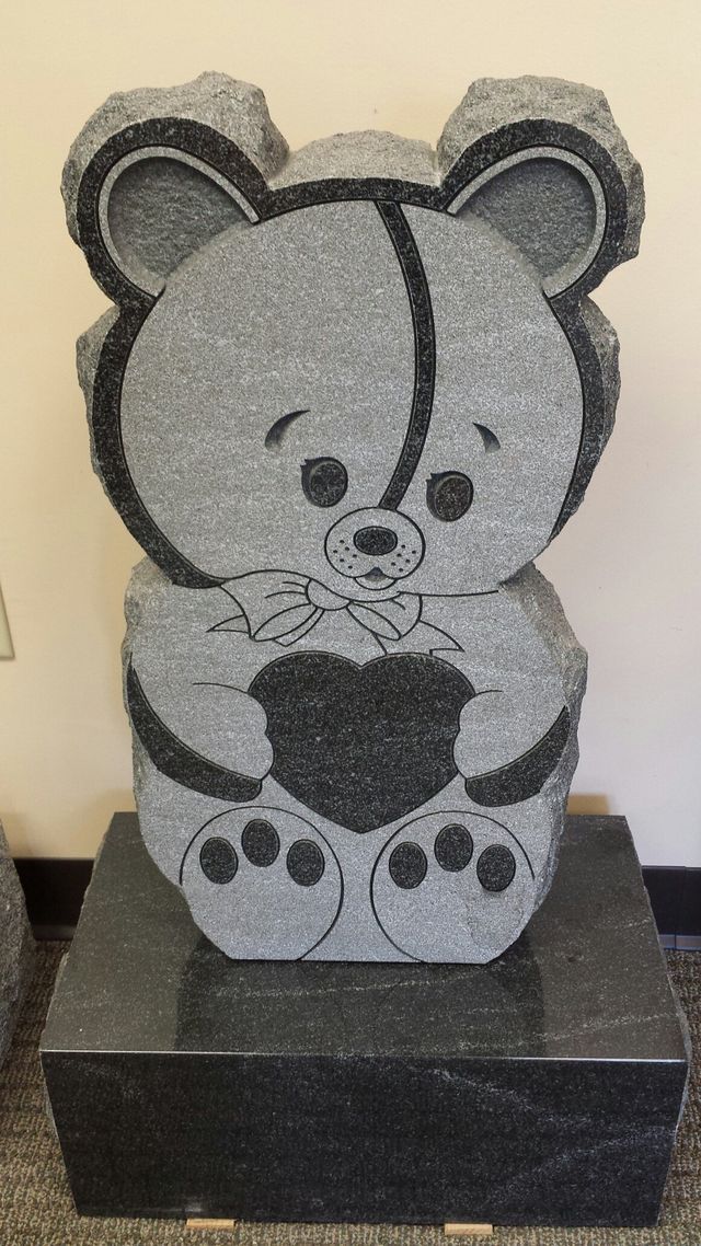 A gravestone in the shape of a teddy bear holding a heart.