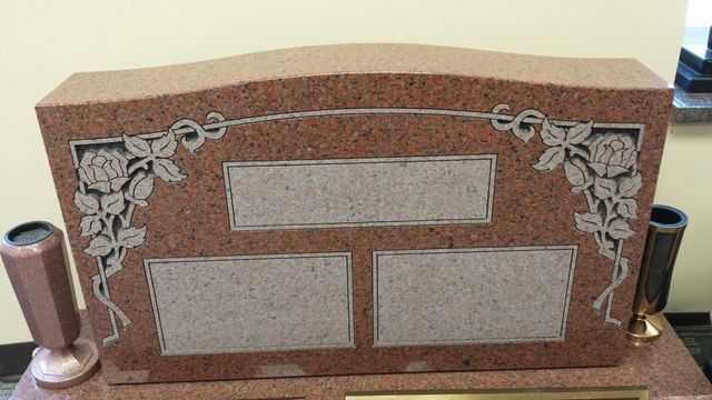 A red granite headstone with two vases on top of it.