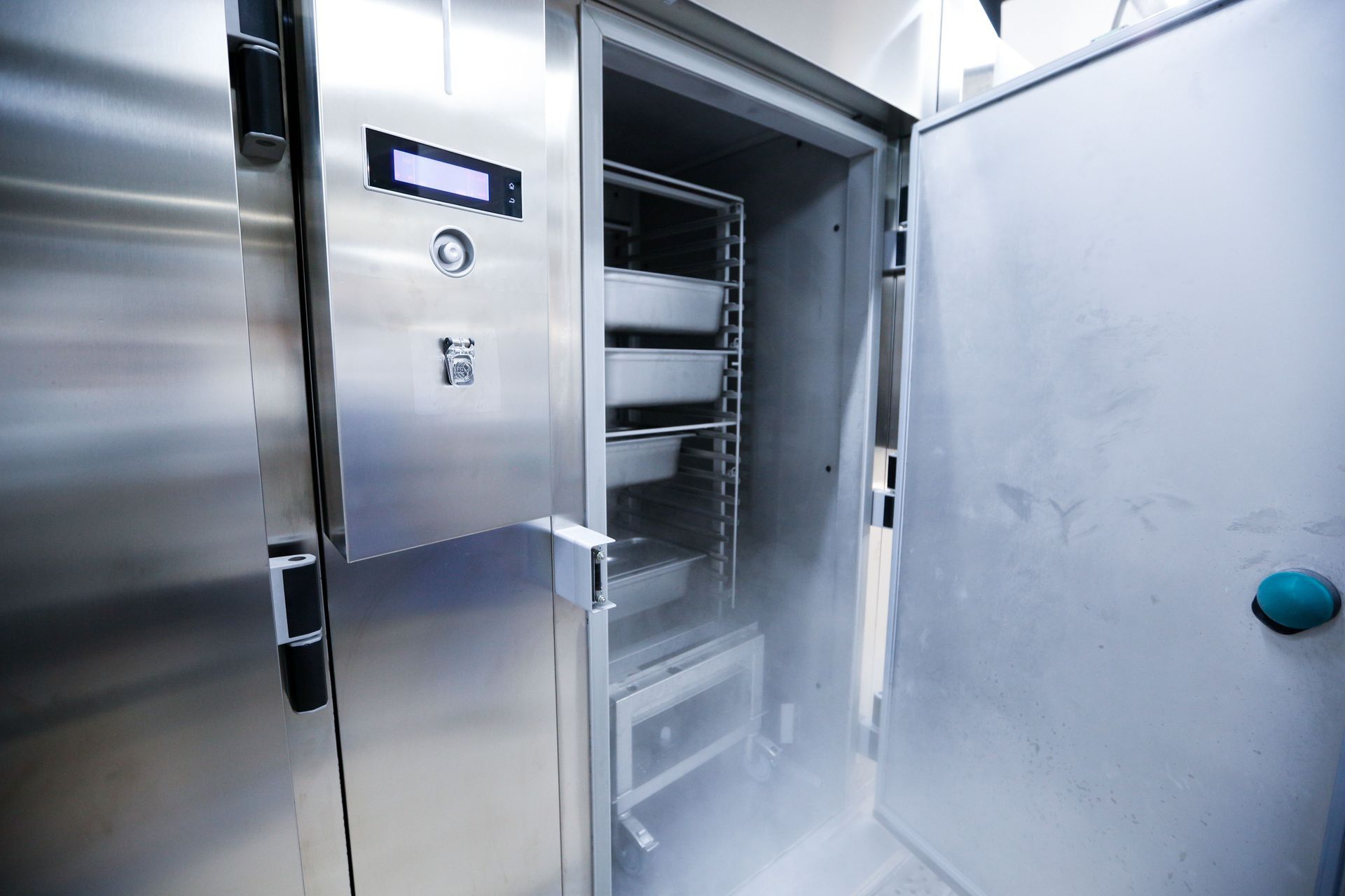 A stainless steel freezer with an open door, revealing shelves and emitting vapor.