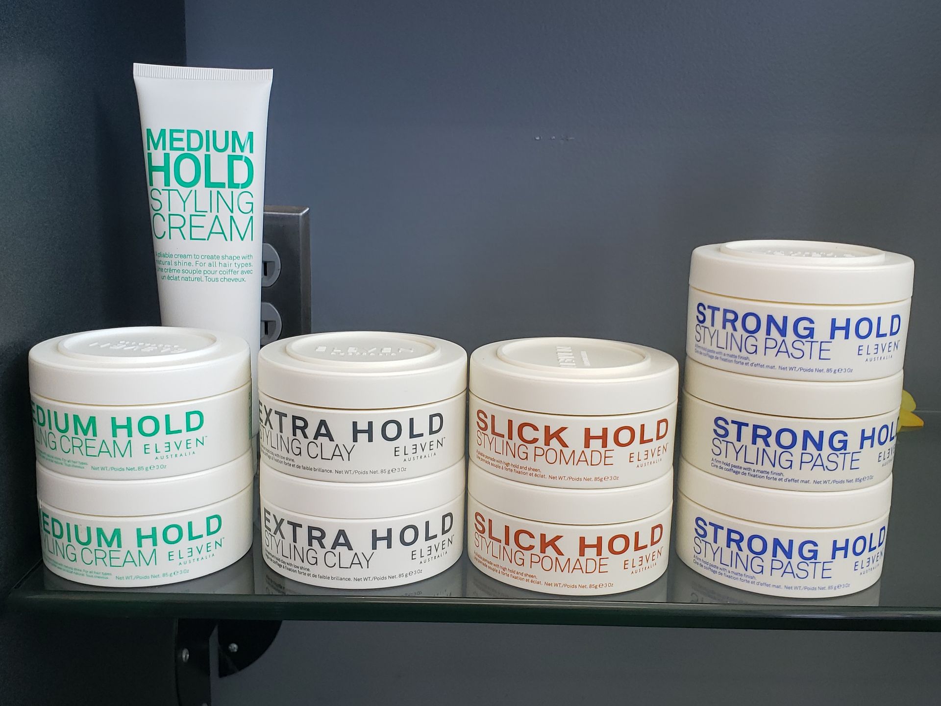 A variety of hair products are sitting on a glass shelf.