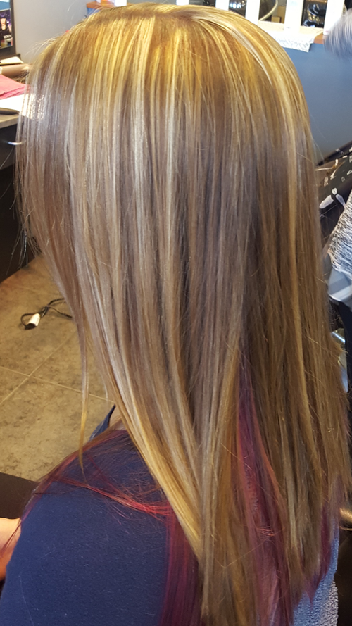 A woman with long blonde hair and red highlights is sitting in a chair.