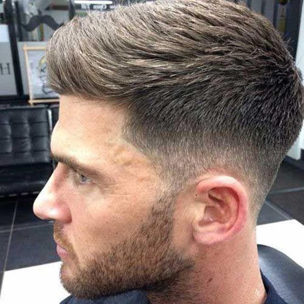 A man with a beard is getting his hair cut at a barber shop.