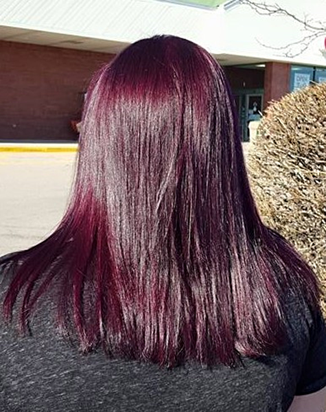 A woman with long burgundy hair is standing in front of a building.
