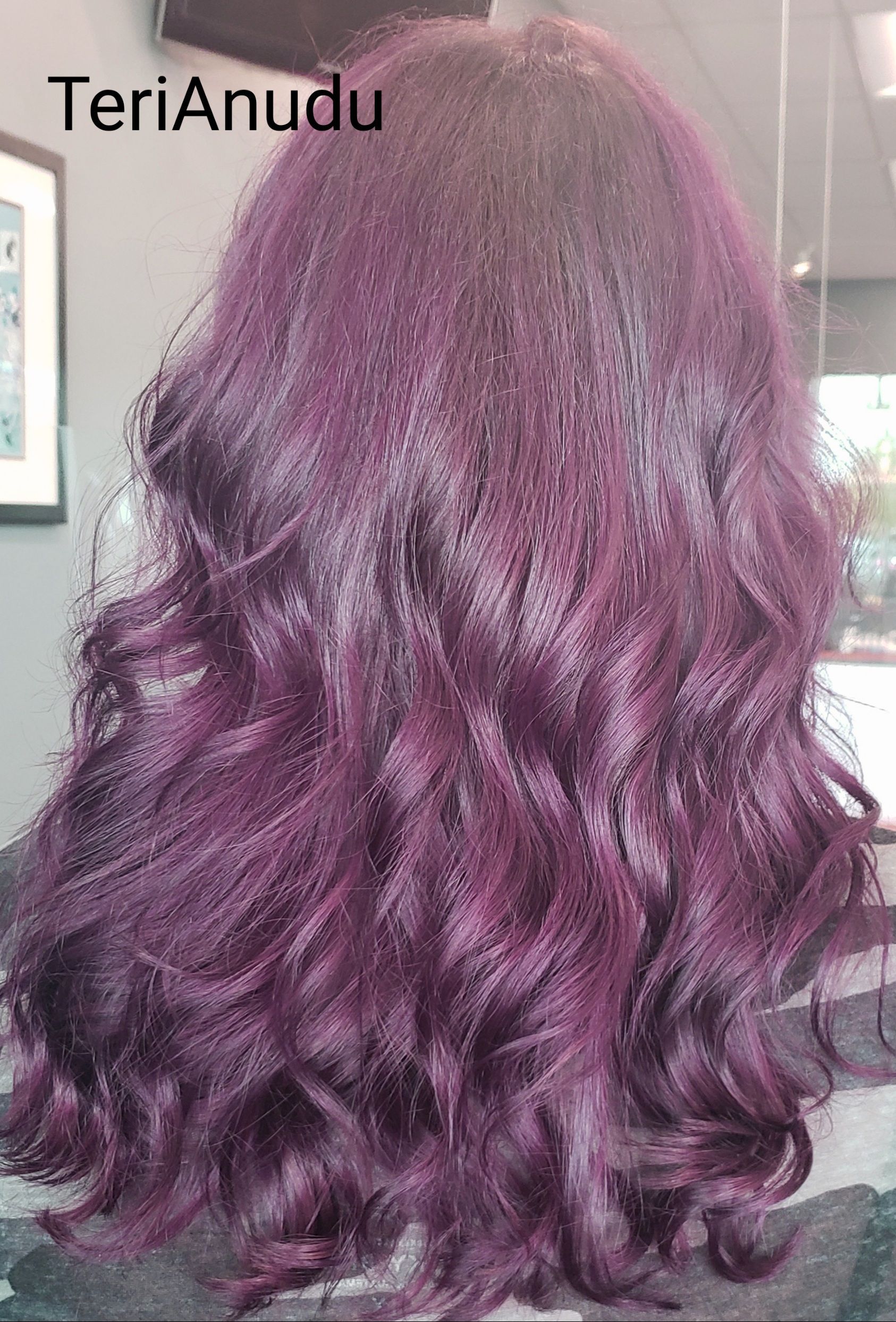 A woman with purple hair is sitting in front of a mirror