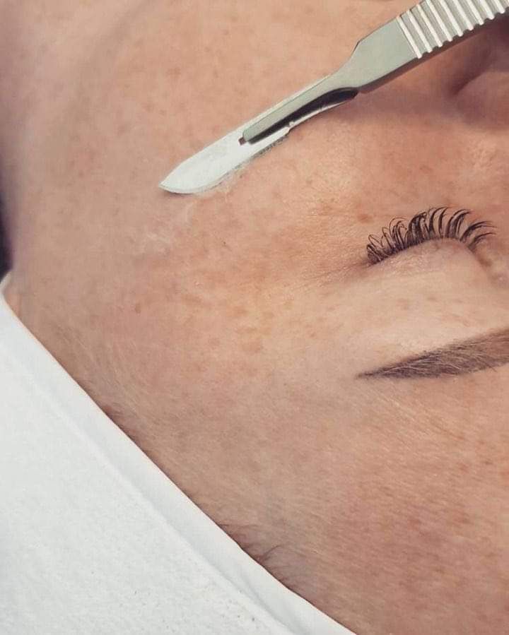 A woman is getting her eyebrows shaved with a scalpel.