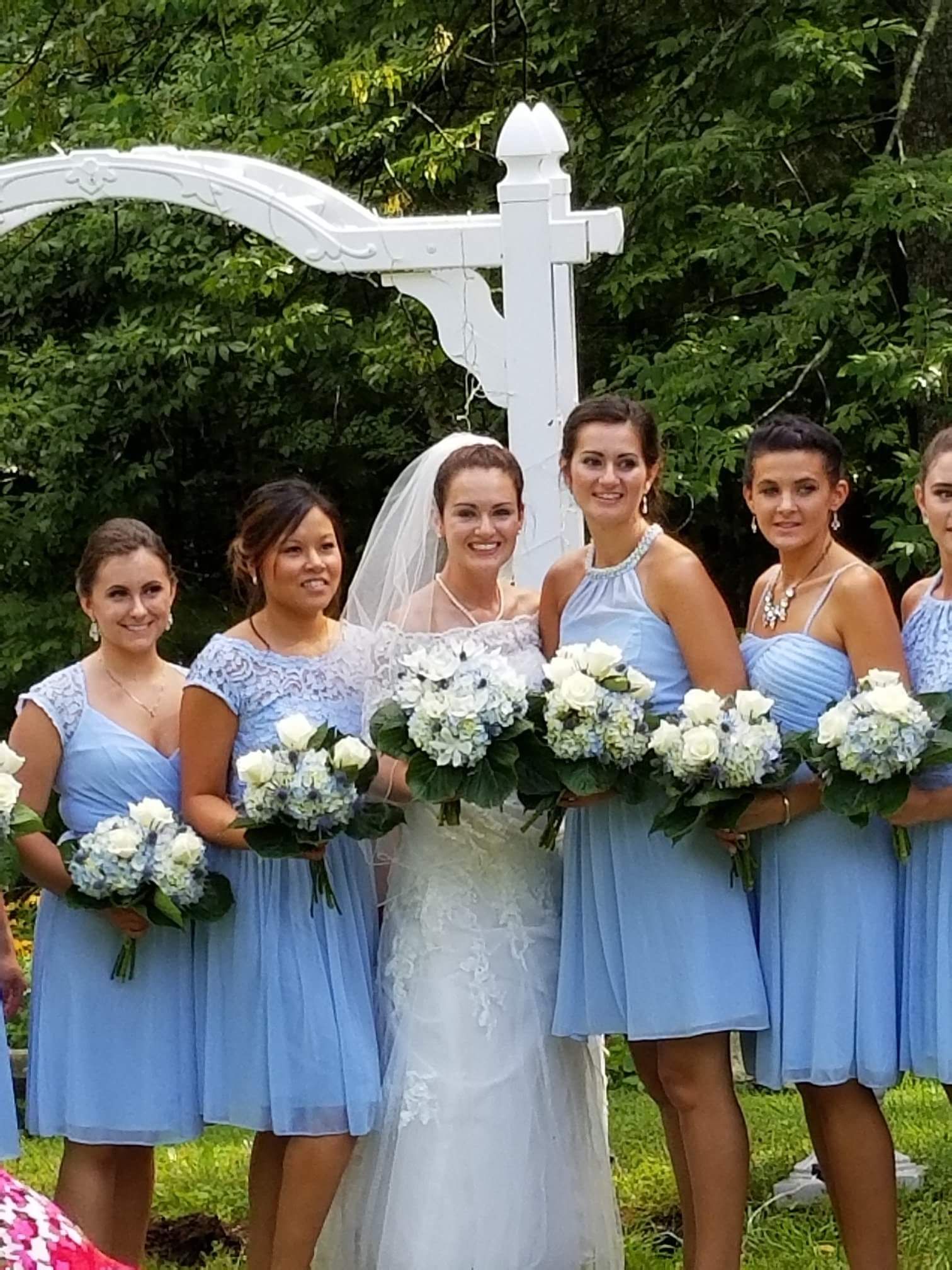 A bride and her bridesmaids are posing for a picture in front of a white arch.