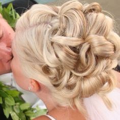 A woman with blonde hair in a bun is kissing a man.