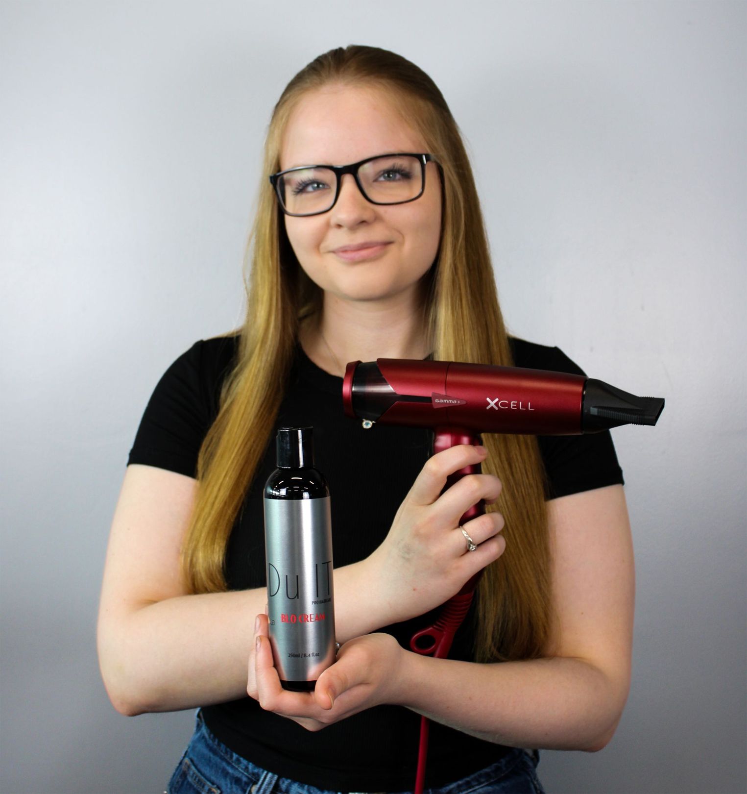A woman is holding a hair dryer and a bottle of shampoo