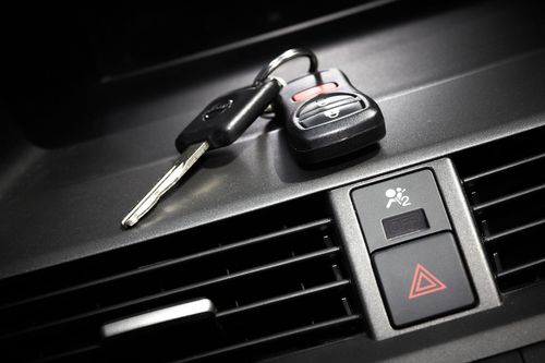 Car keys resting on a car dashboard near the air vent and hazard light button