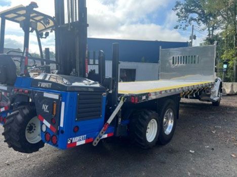 Blue forklift mounted on a flatbed truck, outside. 