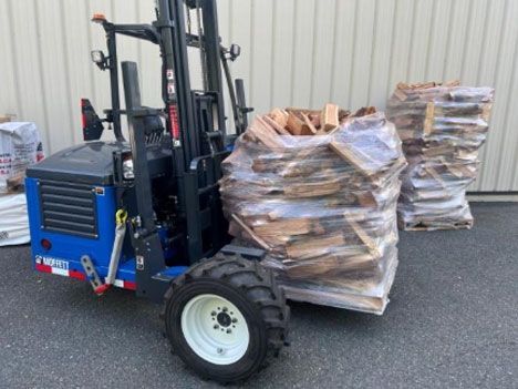 Blue forklift holding wrapped firewood bags; outdoors.