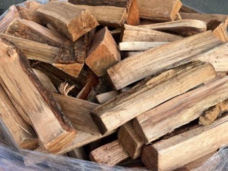 Pile of split firewood, mostly light brown and tan, ready for burning.