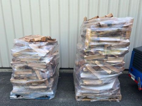 Two pallets of wrapped firewood stacked outside a building.