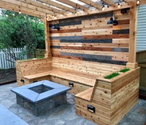 A wooden patio with a fire pit and benches under a pergola.