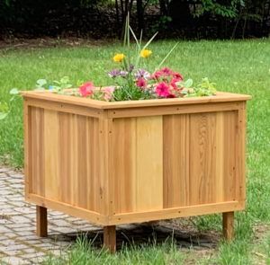 A wooden planter filled with flowers is sitting in the grass.