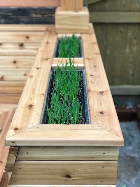 A wooden planter filled with green grass is sitting on top of a wooden deck.