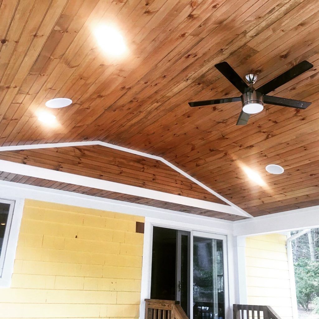 A porch with a wooden ceiling and a ceiling fan.