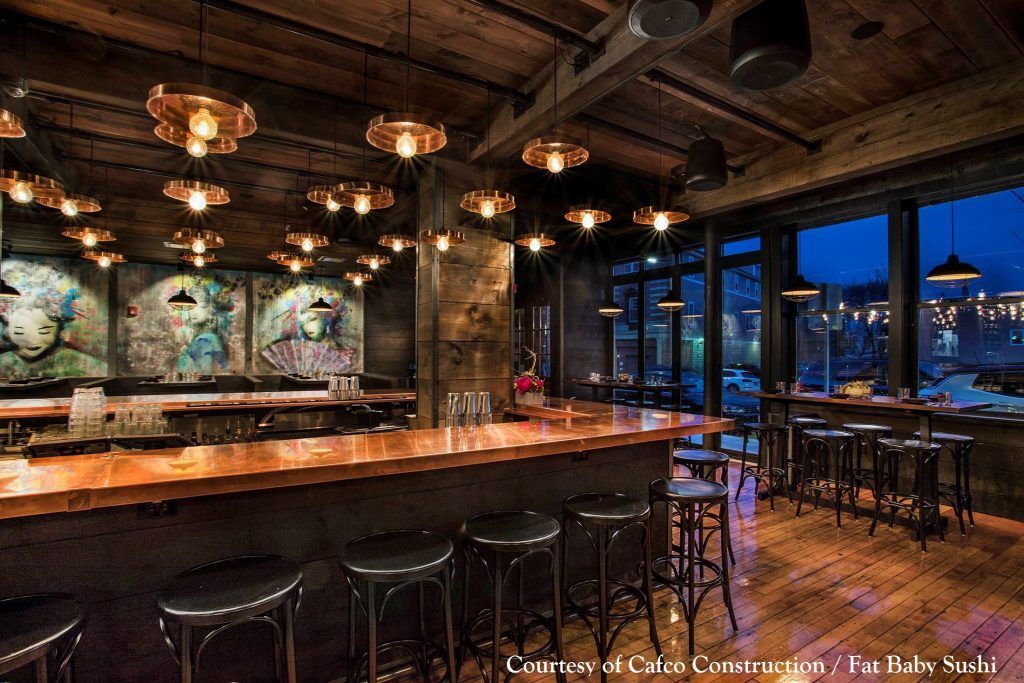 A restaurant with a long bar and stools and a lot of windows.